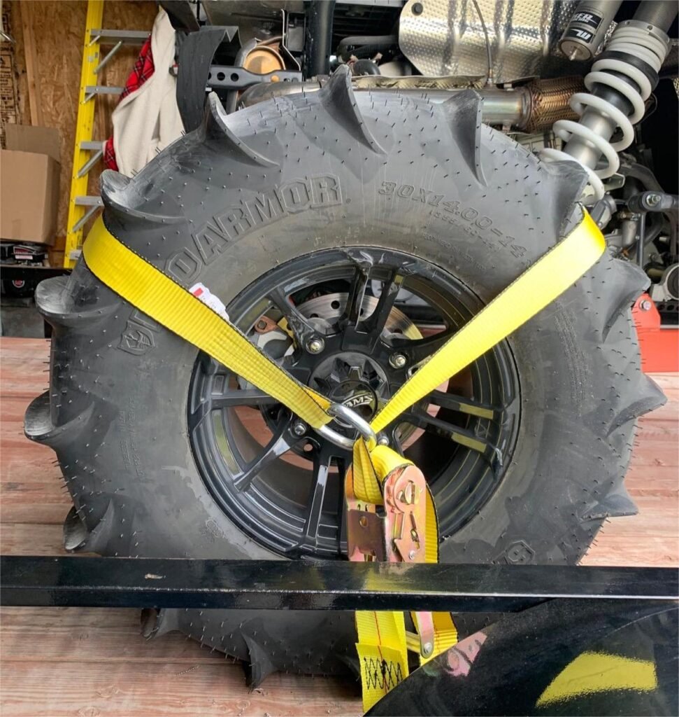 Yellow tie-down straps securing a spare tire in place inside a truck or trailer, preventing movement during transit.